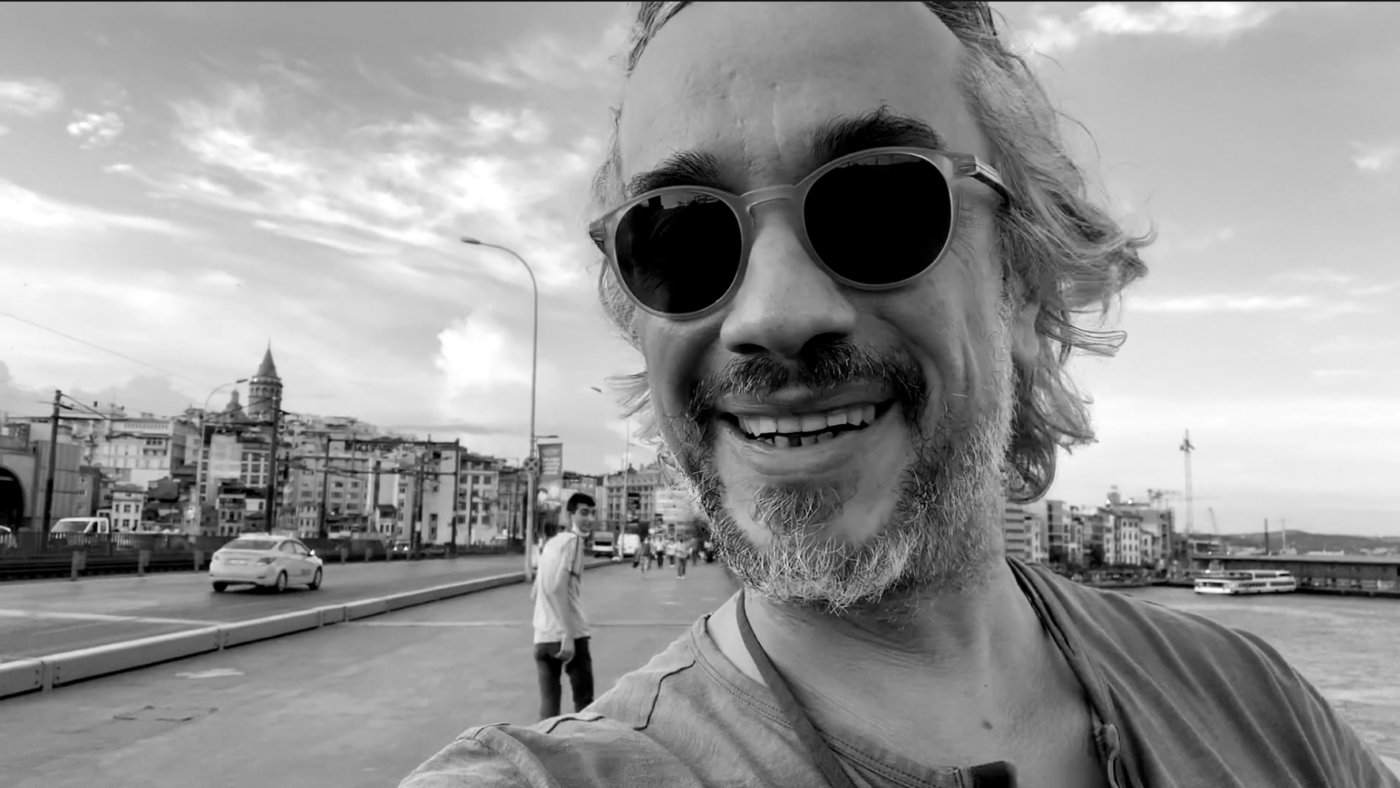 Galata Köprüsü’nde çekilmiş siyah beyaz bir selfie; önde güneş gözlüklü bir adam, arka planda dönüp kameraya bakan bir çocuk ve Galata silueti.